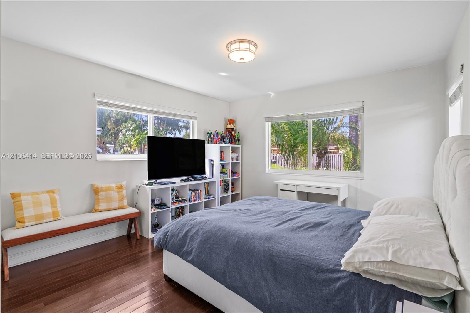 Bedroom featuring wood-finish flooring, dual windows with blinds, and a central flush-mount light fixture
