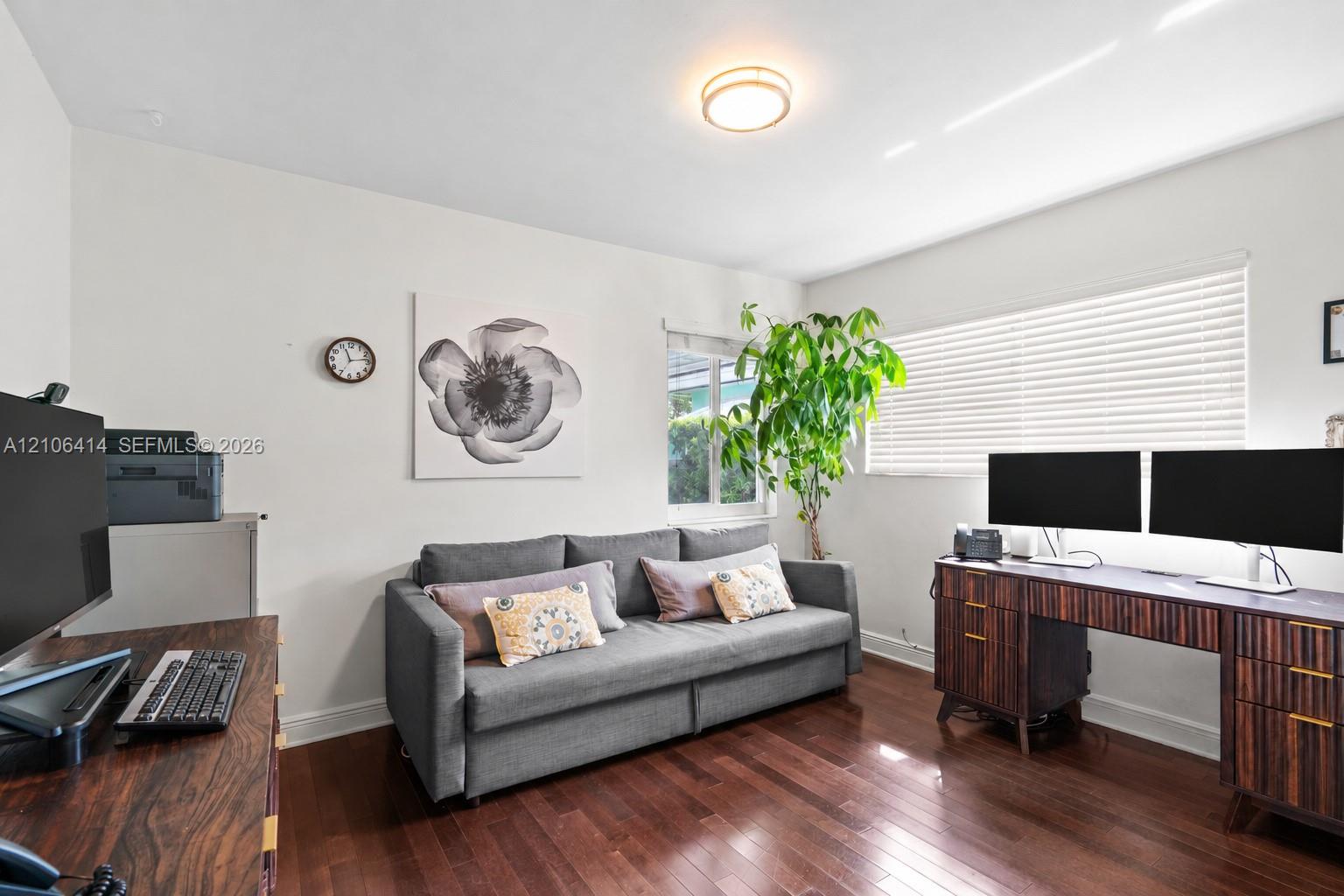 Room featuring wood-finish flooring, dual windows with horizontal blinds, and a central ceiling-mounted light fixture