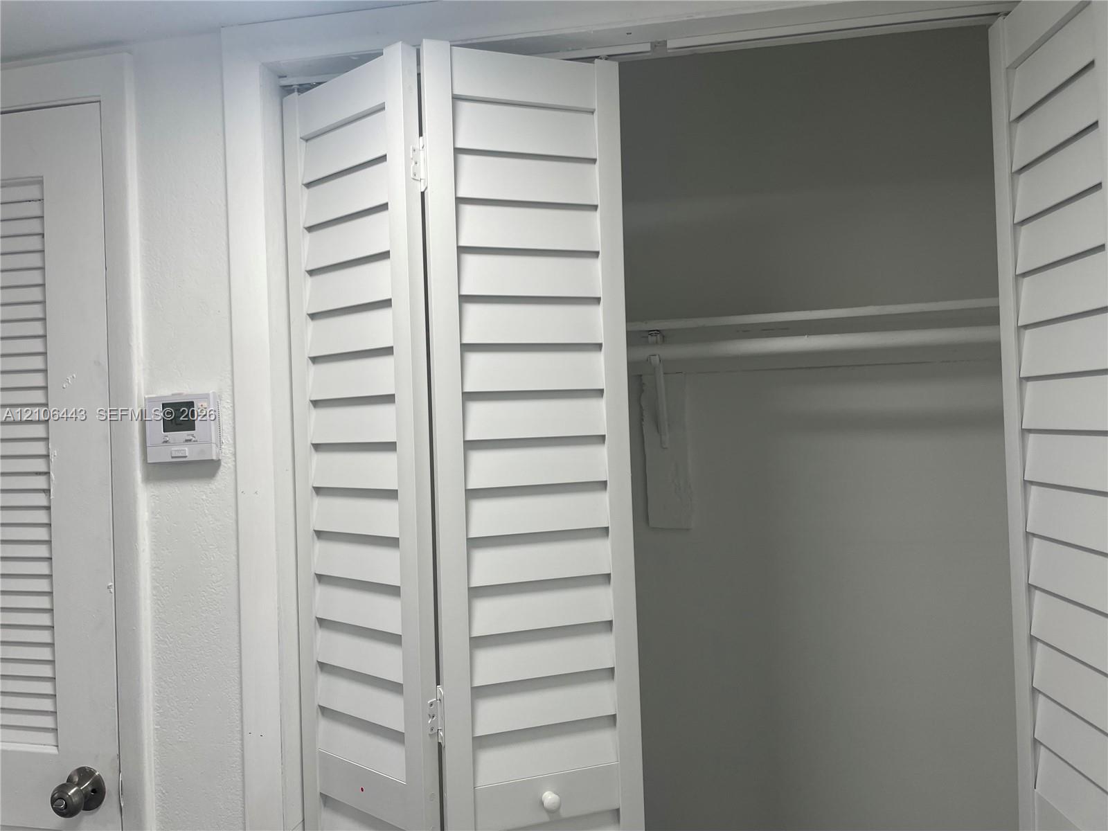 White bi-fold louvered closet doors, interior shelf, and metal garment rod