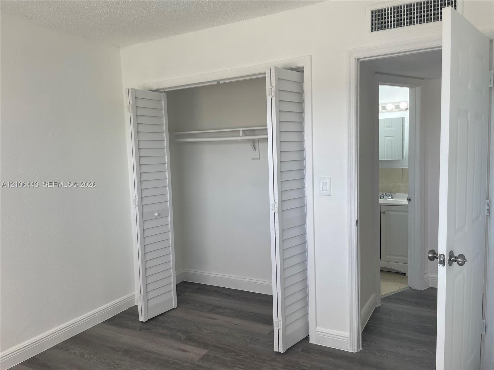 Interior space featuring wood-finish flooring, white louvered closet doors, and solid-core panel doors with brushed nickel hardware