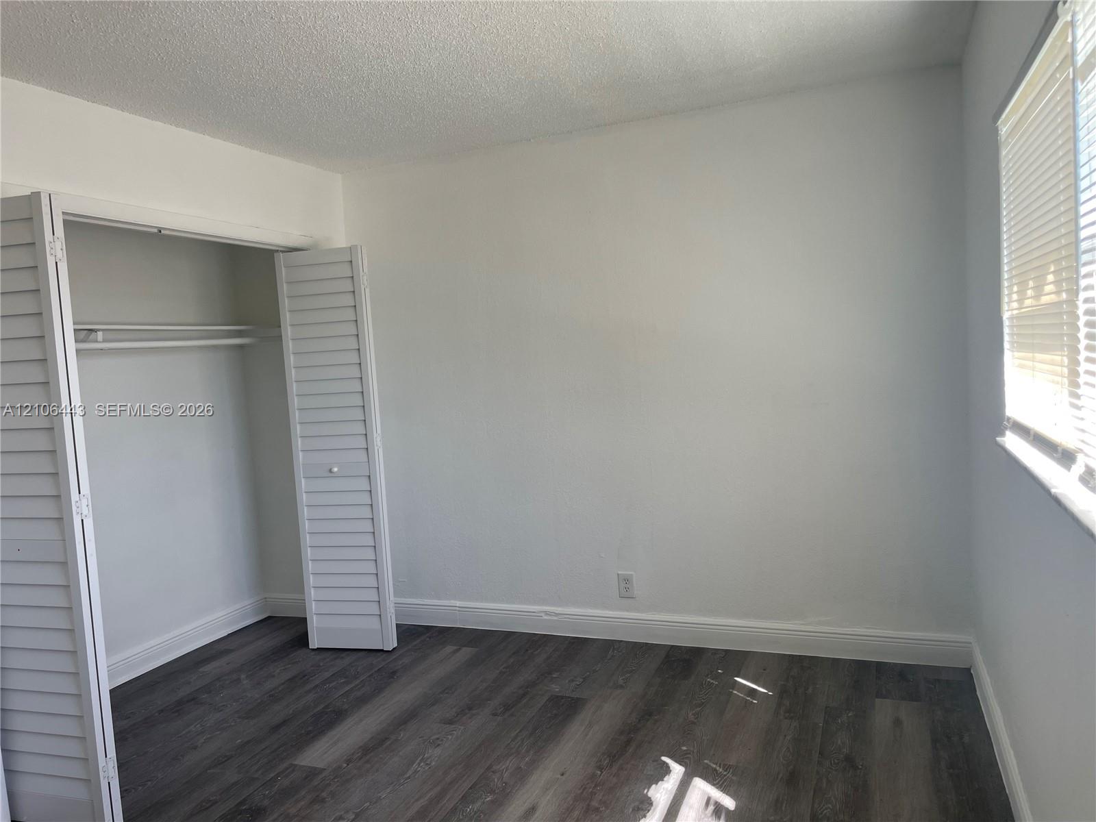 Room featuring wood-finish flooring, white walls, and a closet with louvered bifold doors