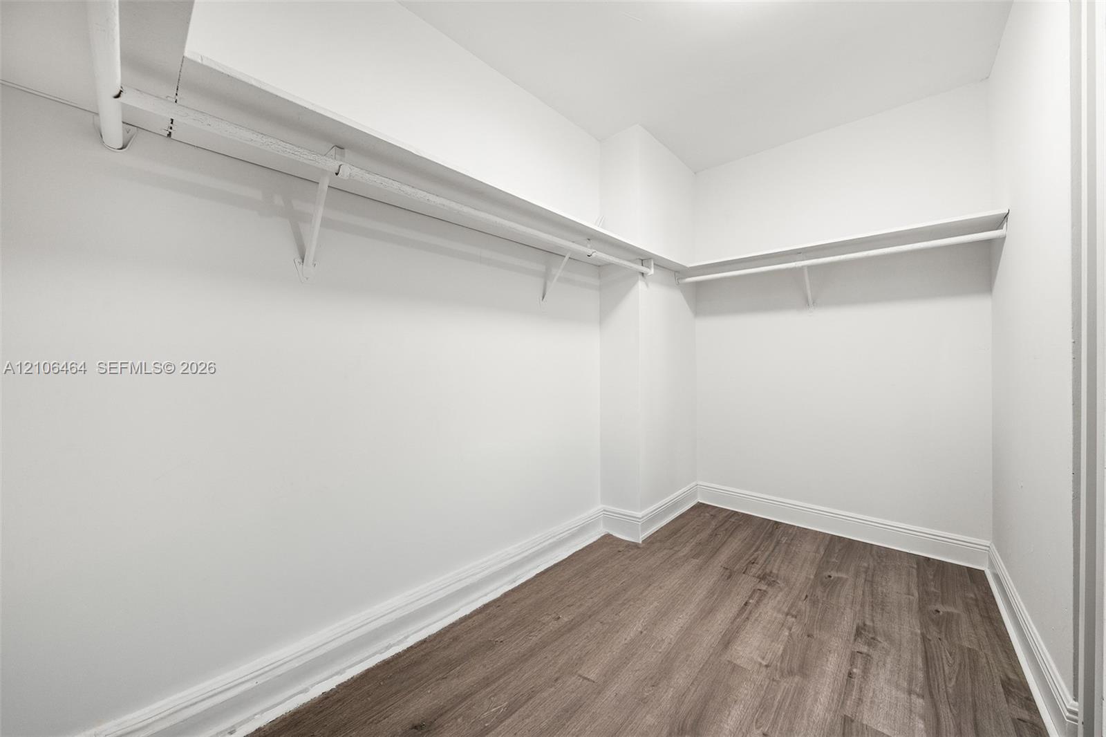 Walk-in storage space featuring wood-finish flooring and integrated hanging rods with overhead shelving