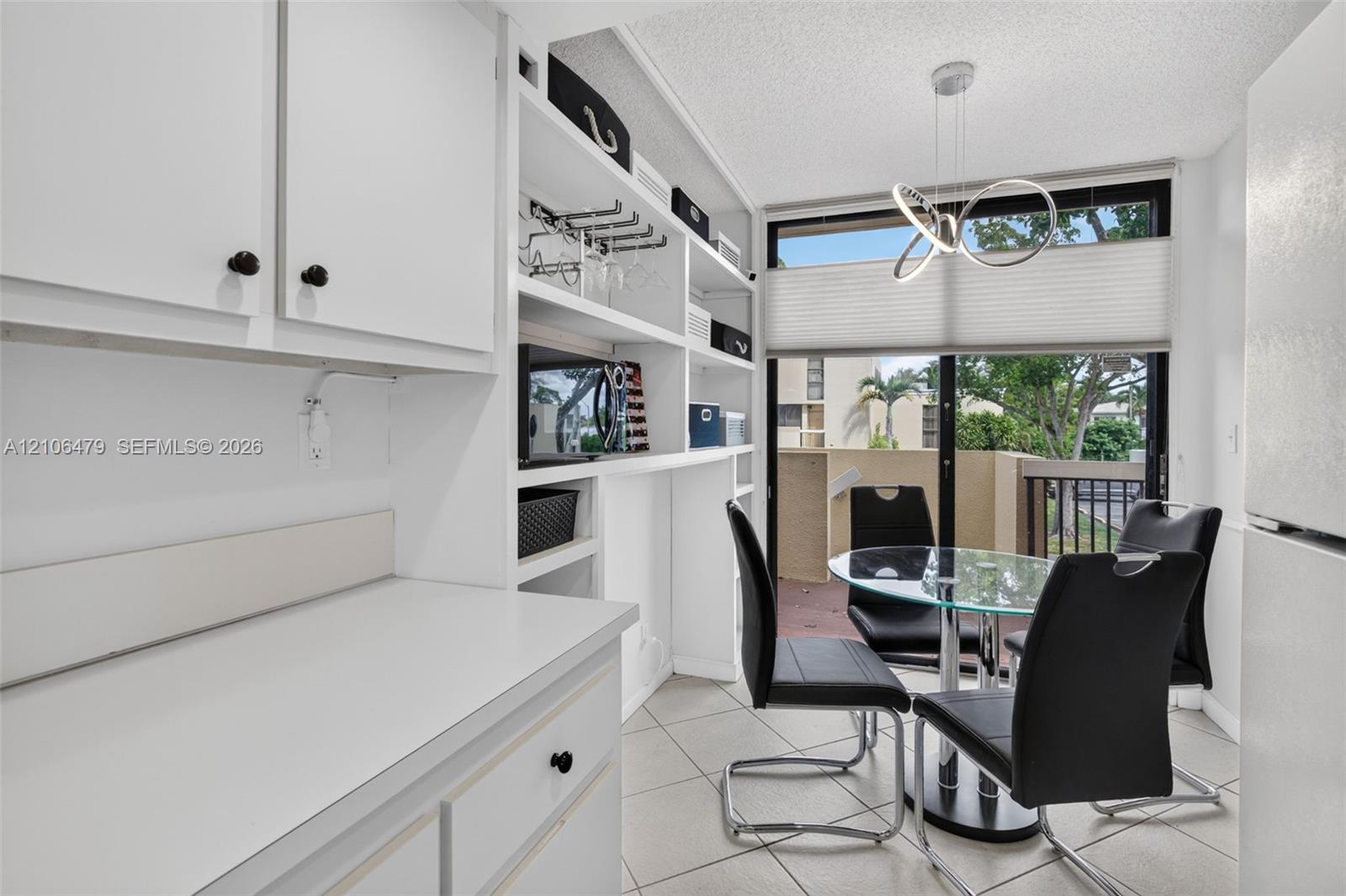 Built-in white cabinetry featuring open shelving, tile flooring, modern sculptural pendant lighting, and sliding glass doors with direct exterior access