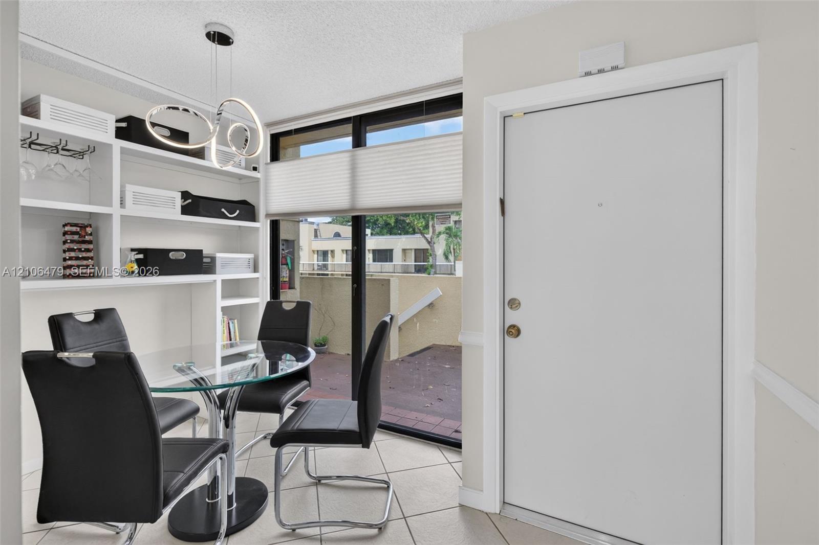 Built-in white shelving, tile flooring, contemporary multi-ring pendant lighting, and large sliding glass door with external patio access