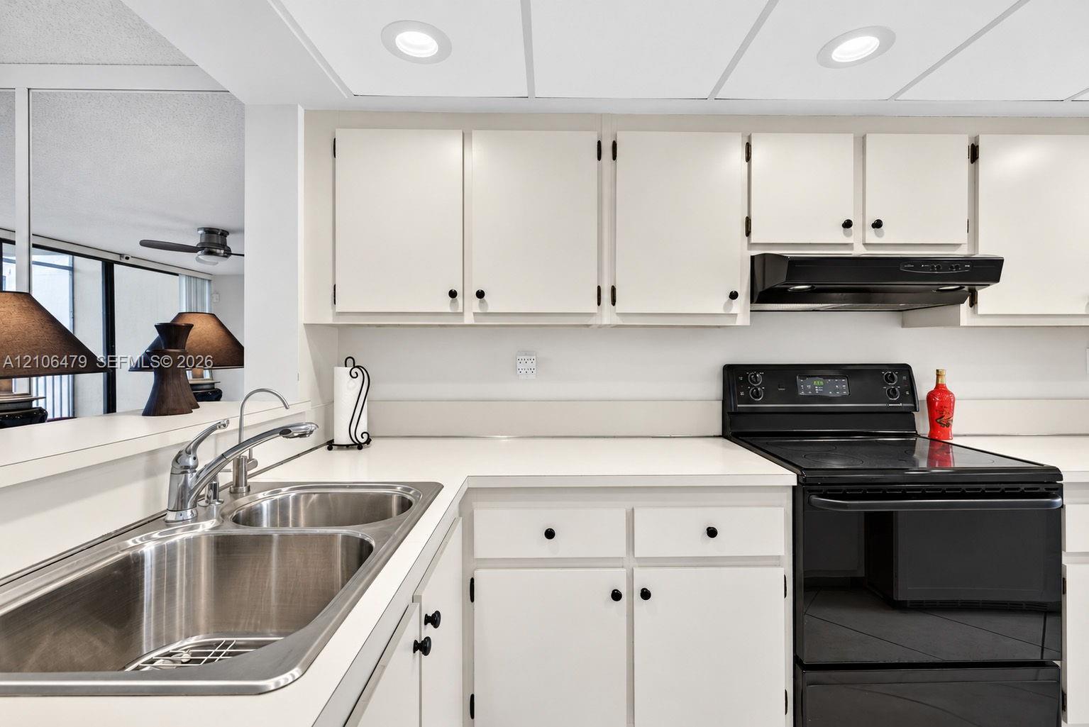 Kitchen featuring white cabinetry, solid-surface countertops, dual-basin stainless steel sink, black range, and recessed ceiling lighting