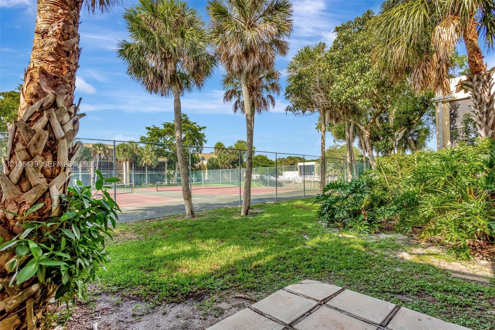 Tennis court with a chain-link fence, concrete patio pavers, and mature palm trees