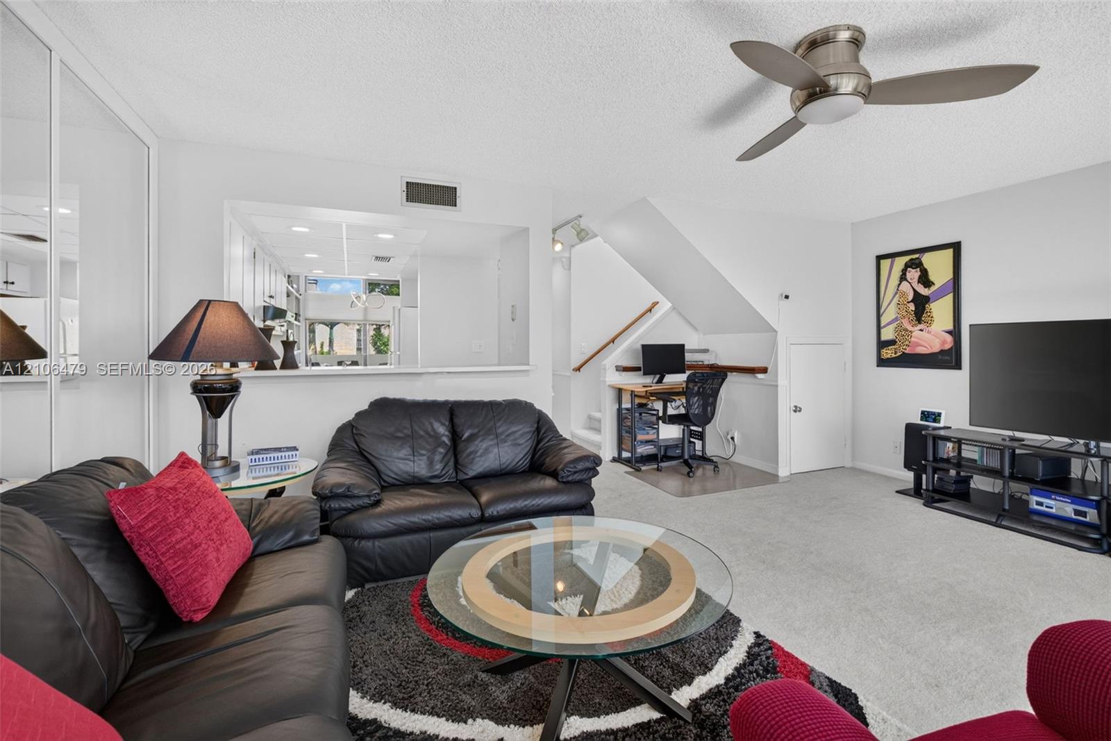 Living area featuring mirrored wall closet doors, a brushed-metal ceiling fan with integrated lighting, and an open pass-through window to the kitchen