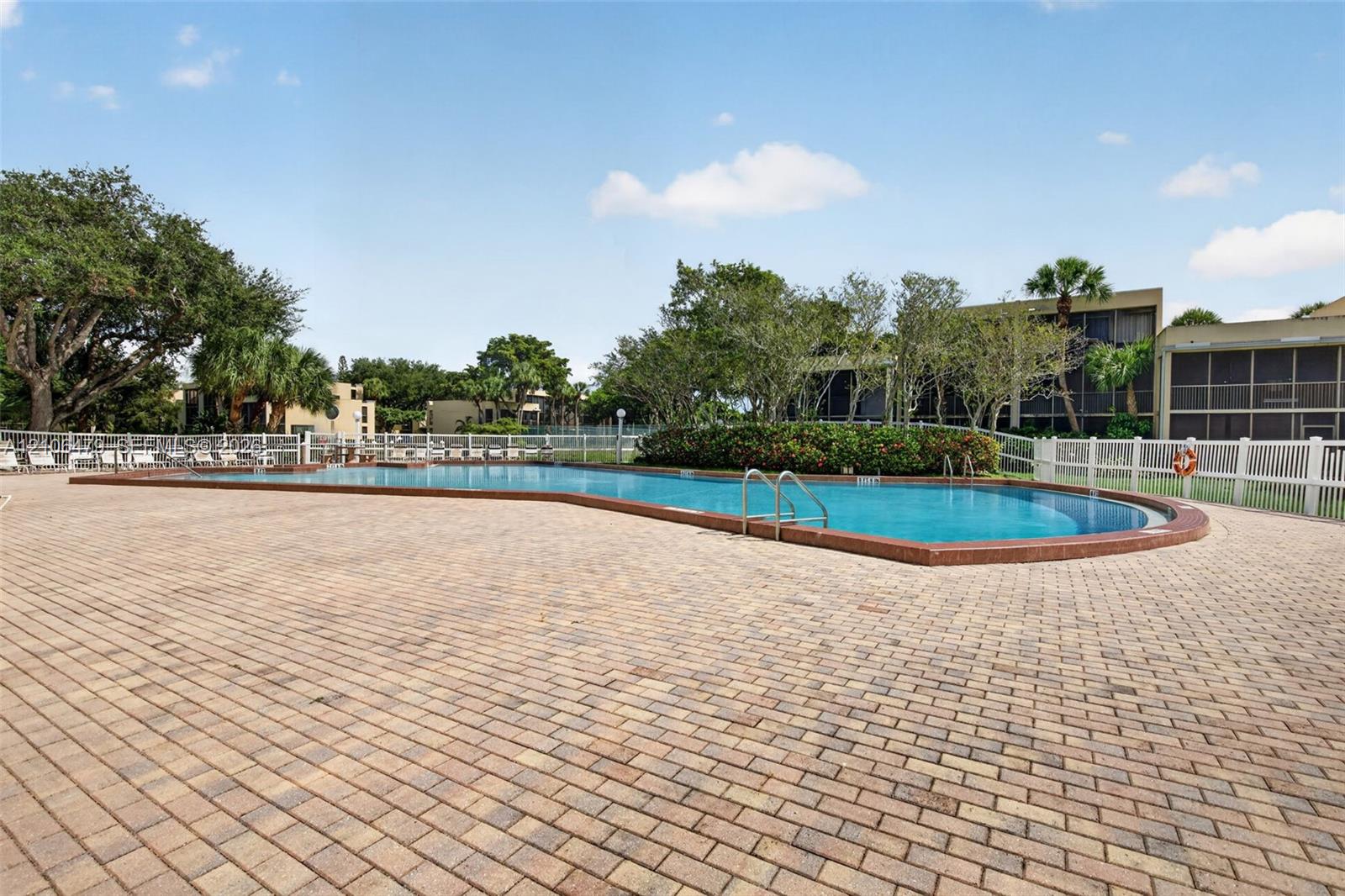 In-ground swimming pool with a brick coping surround and expansive paver deck enclosed by white fencing