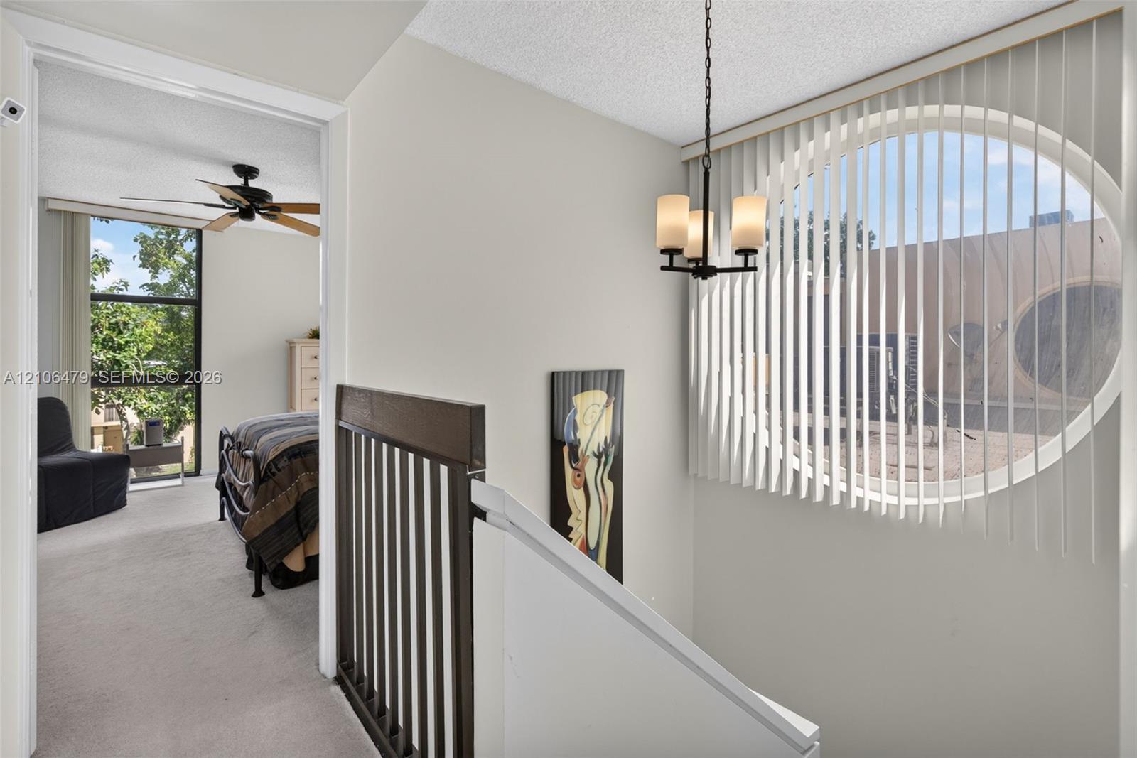 Oval window with vertical blinds, three-light metal chandelier, and decorative wood-finish stair railing