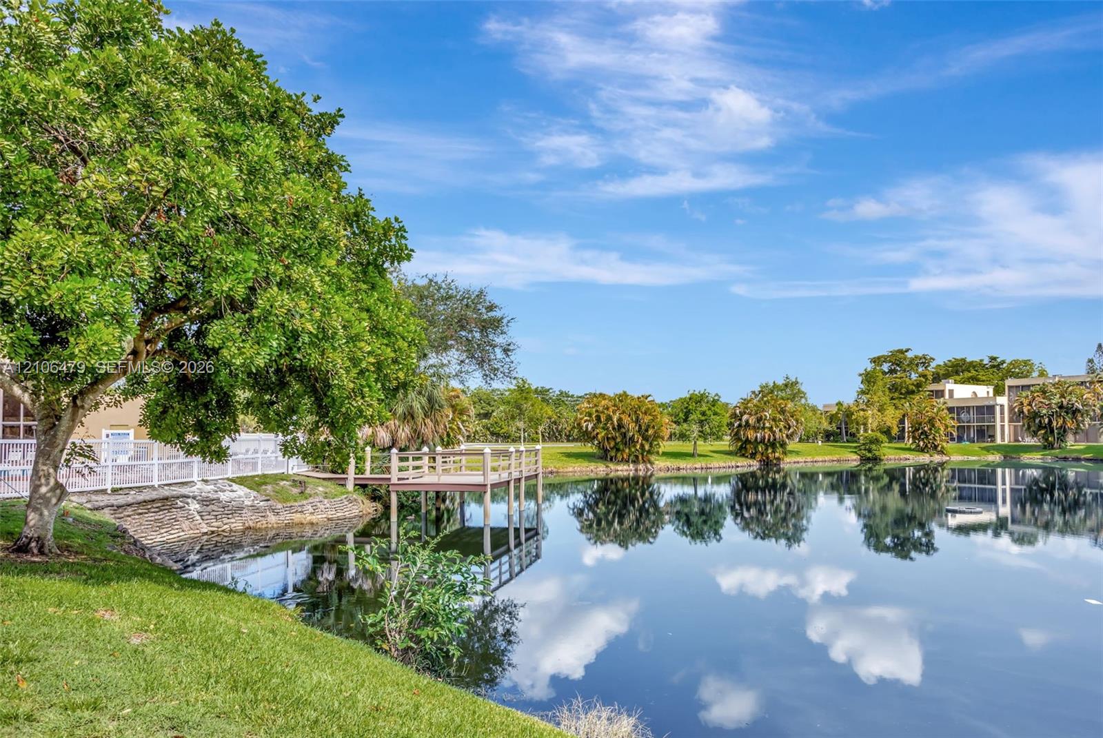 Waterfront grounds featuring a private wooden dock, manicured lawn, mature trees, and stone-reinforced shoreline
