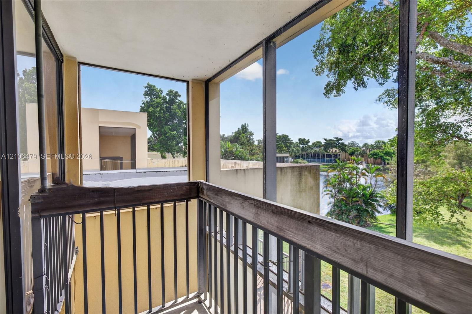 Screened balcony featuring metal railings and wood-finish cap rails overlooking a pond and landscape