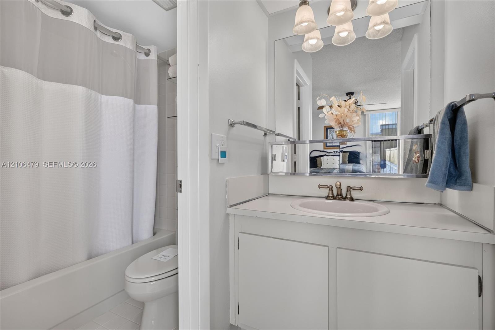 Bathroom featuring a white vanity with integrated sink, metallic widespread faucet, expansive wall-mounted mirror, overhead multi-light fixture, and a combination tub and shower