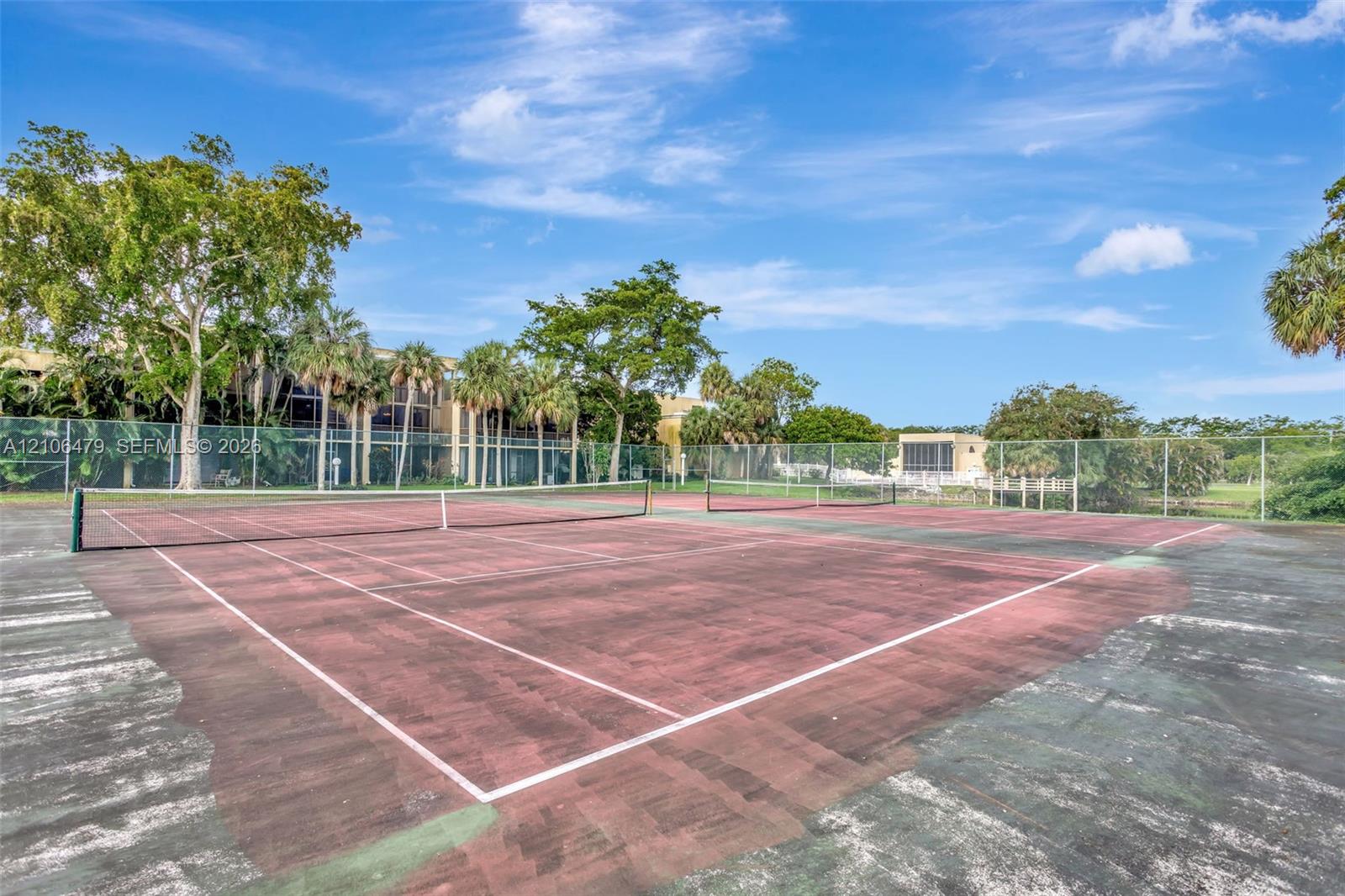 Tennis court featuring a hard surface, perimeter chain-link fencing, and mature landscaping