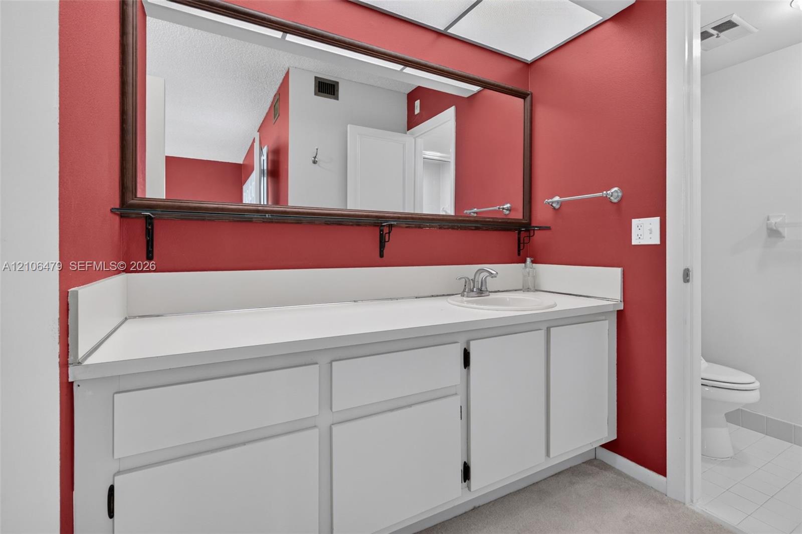 Bathroom featuring a vanity with white cabinetry, a solid surface countertop with an integrated basin, a large wall-mounted mirror with a wood frame, and a separate water closet area