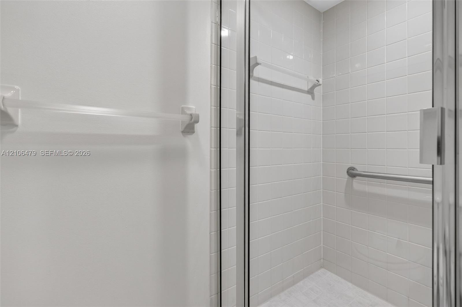 Shower enclosure featuring white wall tiling, a glass door, a wall-mounted metal grab bar, and a horizontal towel rack
