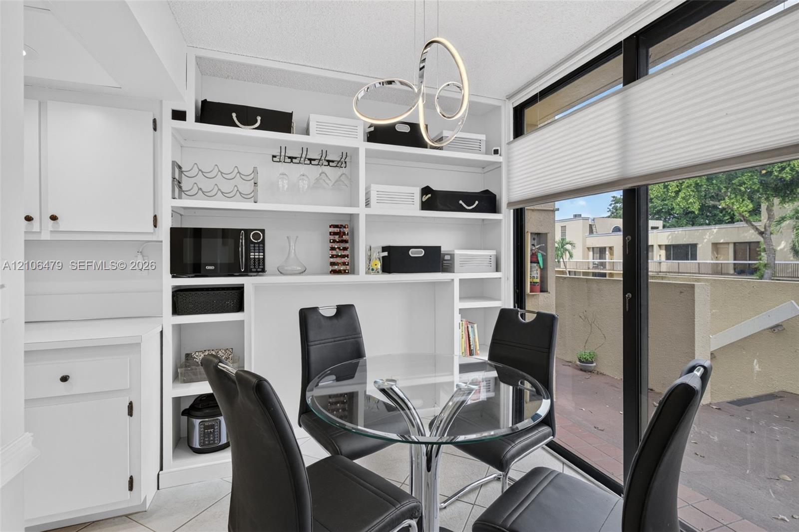 Built-in floor-to-ceiling white shelving unit, contemporary sculptural pendant light fixture, and sliding glass door with integrated cellular shades
