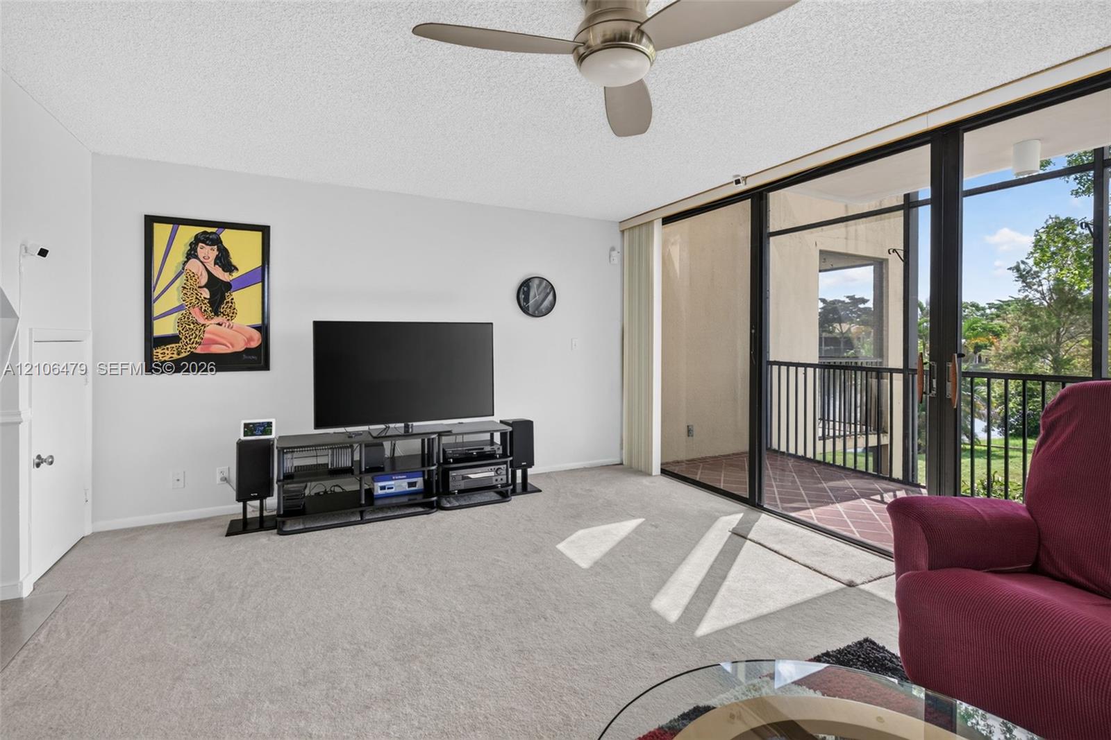 Living area featuring wall-to-wall carpeting, a ceiling-mounted fan, and floor-to-ceiling sliding glass doors providing access to a screened-in balcony with tile flooring and metal railings