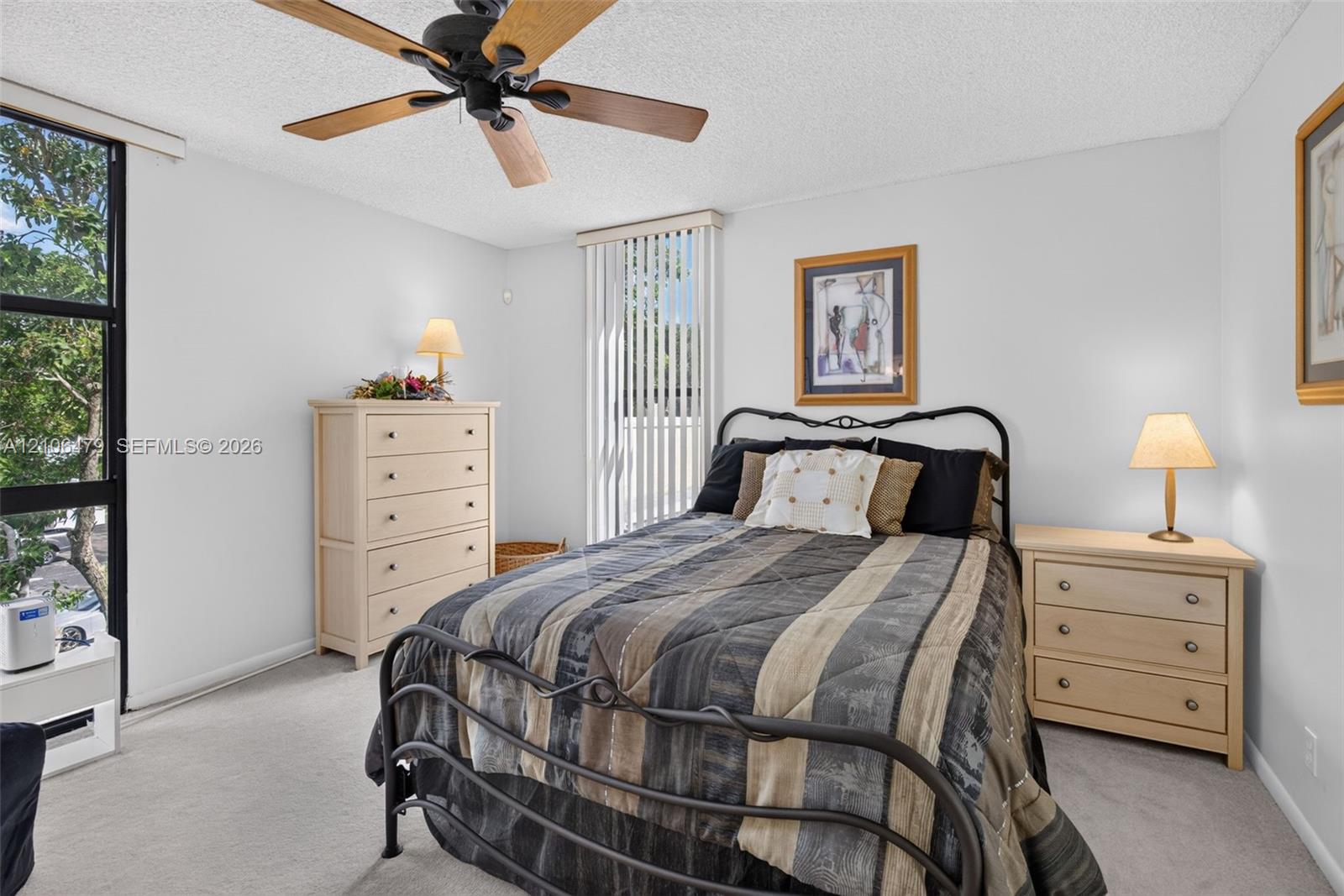 Interior space featuring neutral carpeting, a black-finished ceiling fan with wood-toned blades, floor-to-ceiling black-framed windows, and vertical blinds