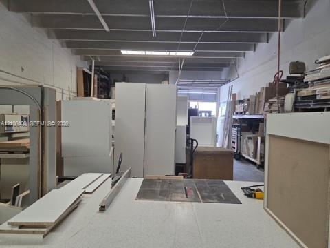 Open-concept workspace featuring exposed structural joists, high ceilings, white-painted masonry walls, and industrial-style linear lighting