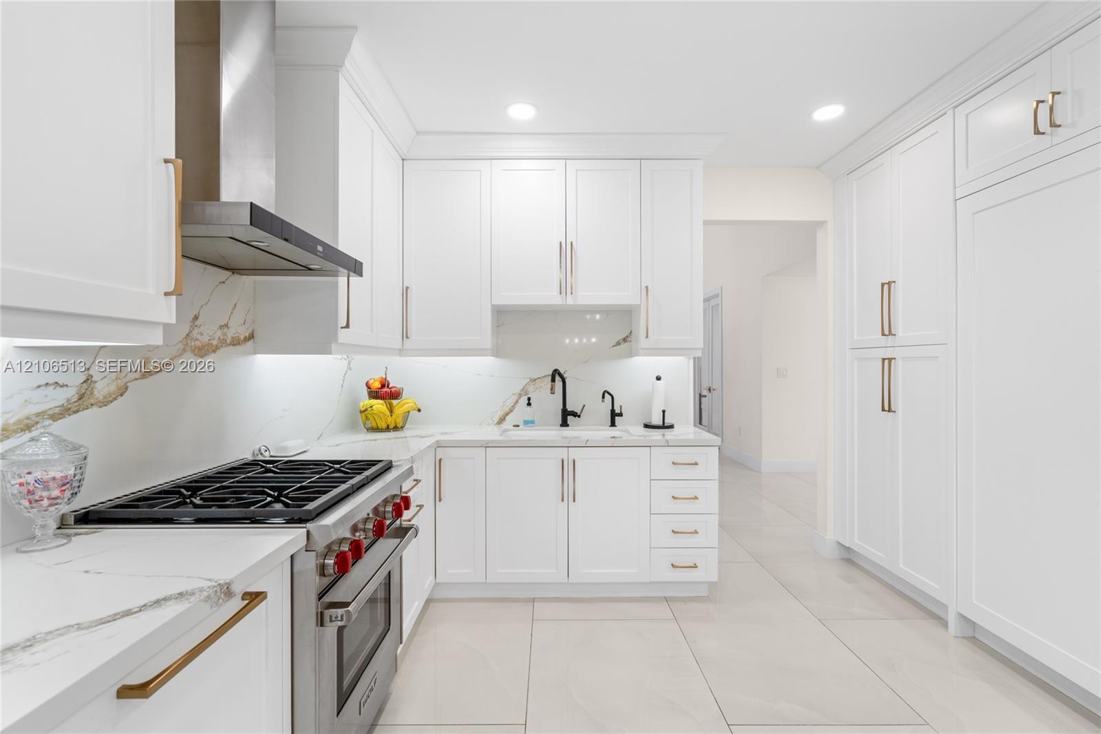 Kitchen featuring shaker-style white cabinetry, stone-finish countertops with matching full-height backsplash, stainless steel gas range with overhead vent hood, under-cabinet lighting, and large-format tile flooring