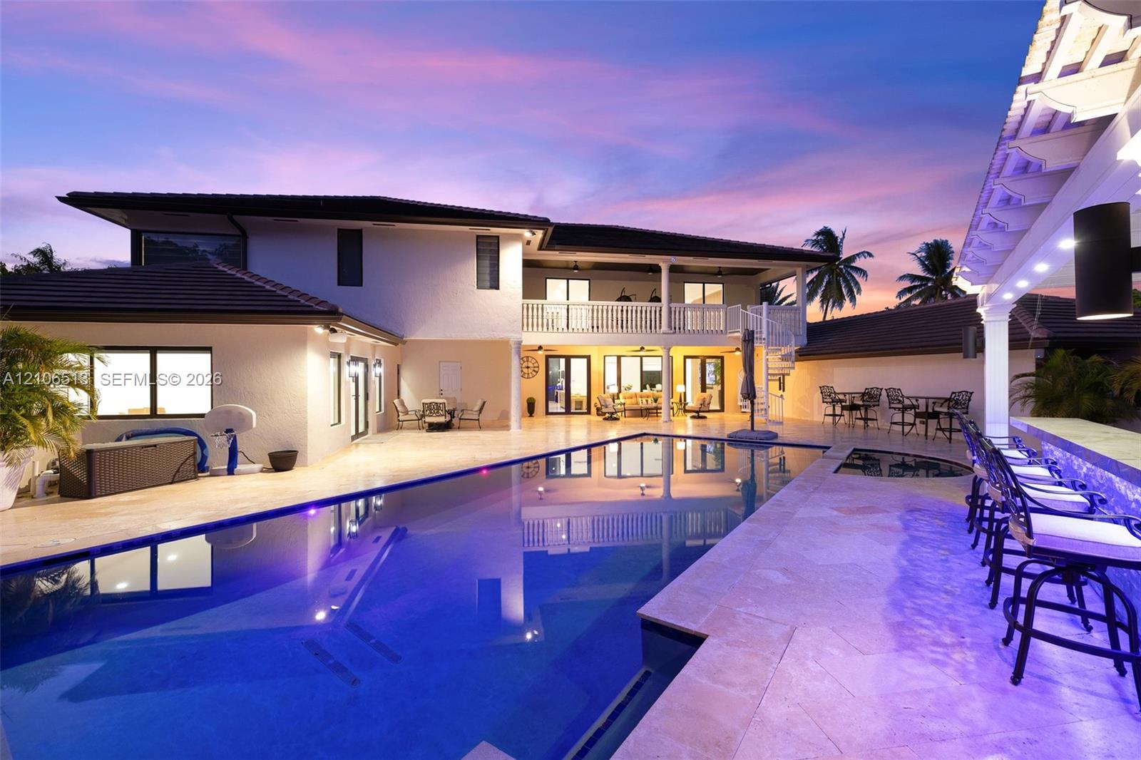 Rear exterior featuring a custom swimming pool with integrated spa, stone-paver decking, built-in swim-up bar, and second-level balcony with white railings