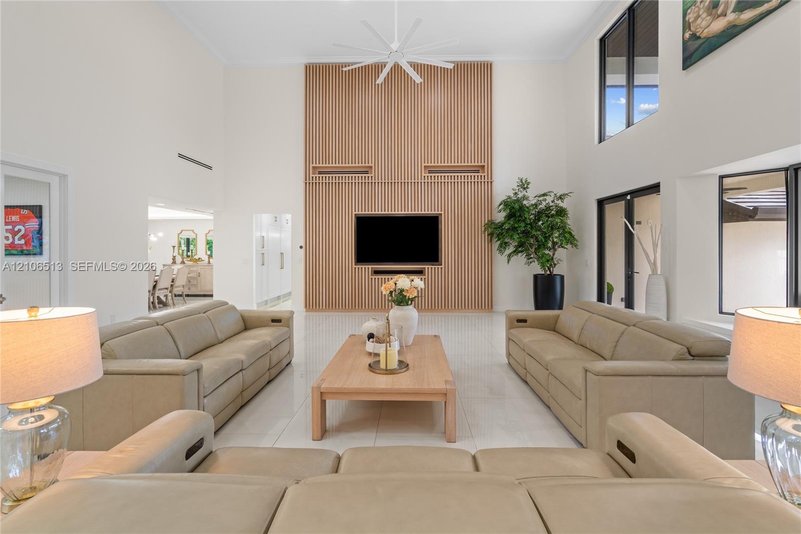 Double-height ceiling, wood-slat accent wall, large-format tile flooring, oversized windows, and multi-blade ceiling fan