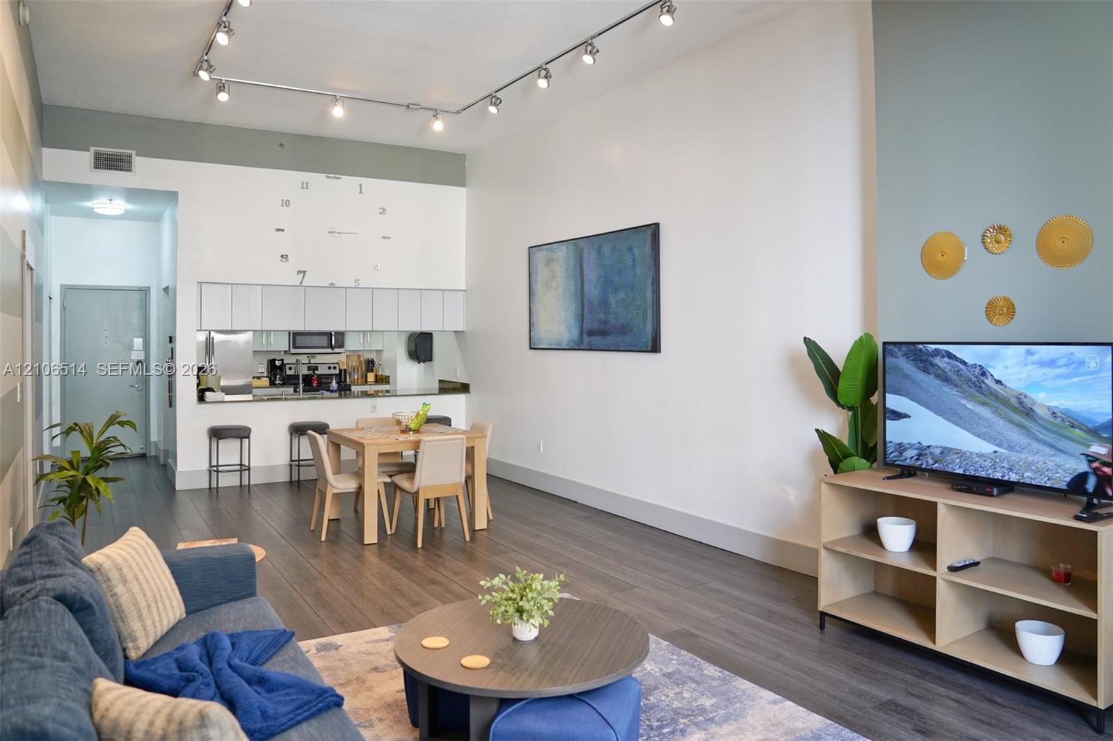 High ceilings featuring a linear track lighting system, dark wood-finish flooring, and a kitchen with overhead cabinetry