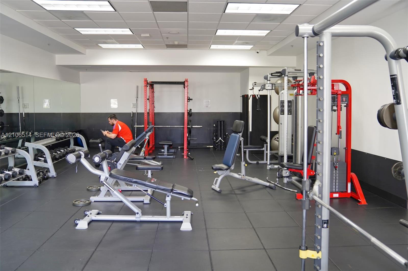 Fitness center featuring rubberized flooring, floor-to-ceiling wall mirrors, and a suspended drop ceiling with recessed lighting