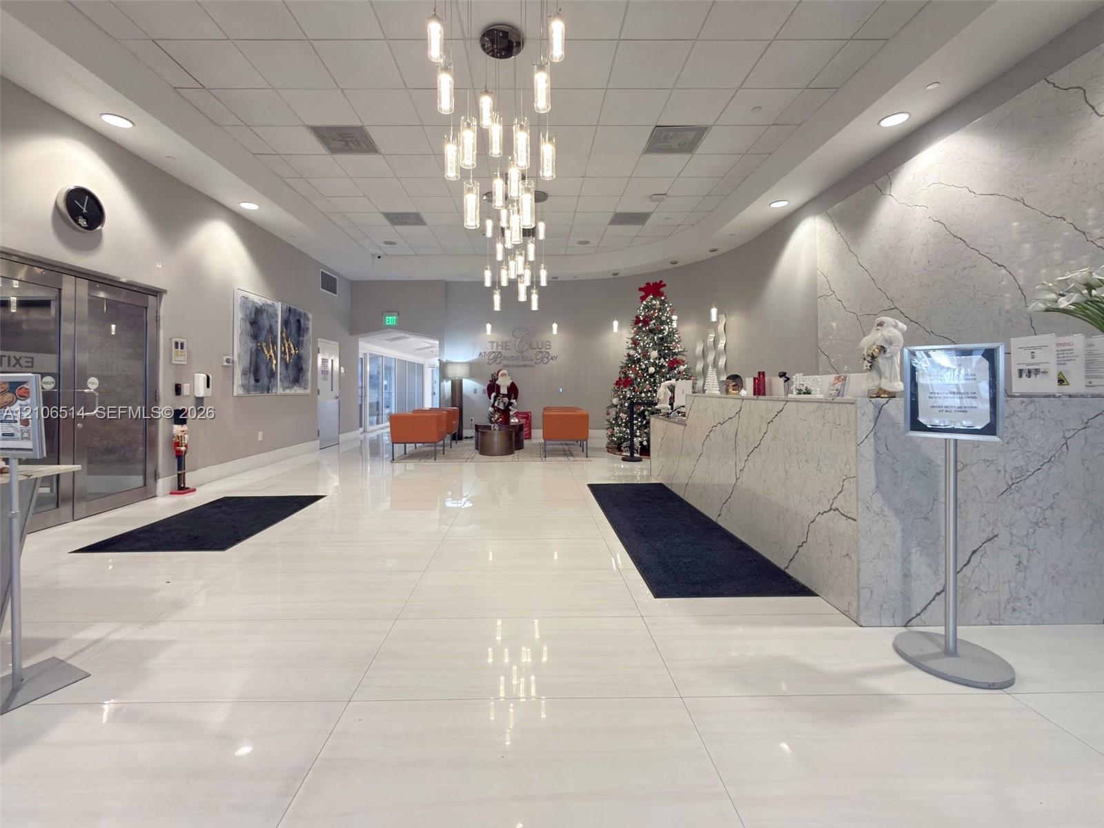 Grand lobby featuring polished tile flooring, a multi-tiered glass pendant chandelier, and a reception desk finished in stone surfacing with veining detail