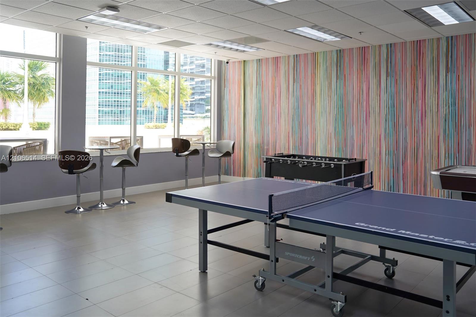 Expansive multi-purpose space featuring full-height floor-to-ceiling windows, high-contrast patterned wall covering, recessed ceiling lighting, and neutral tile flooring