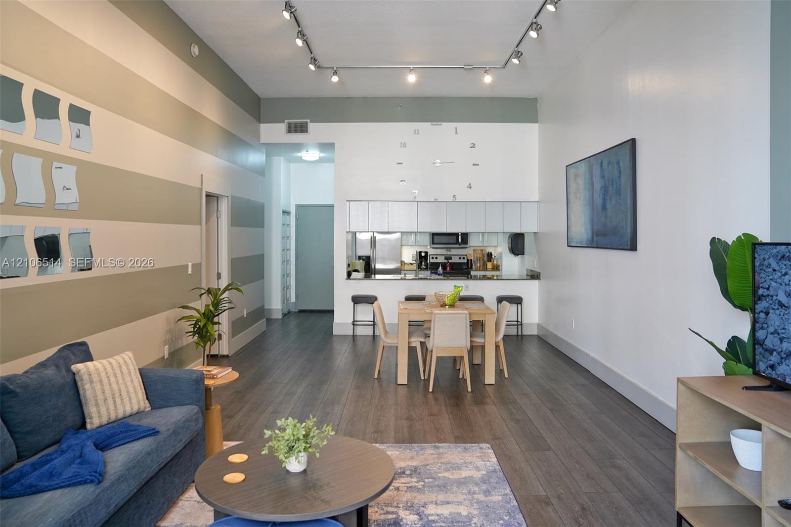 Open-concept interior featuring high ceilings, wood-finish flooring, track lighting, and built-in upper cabinetry