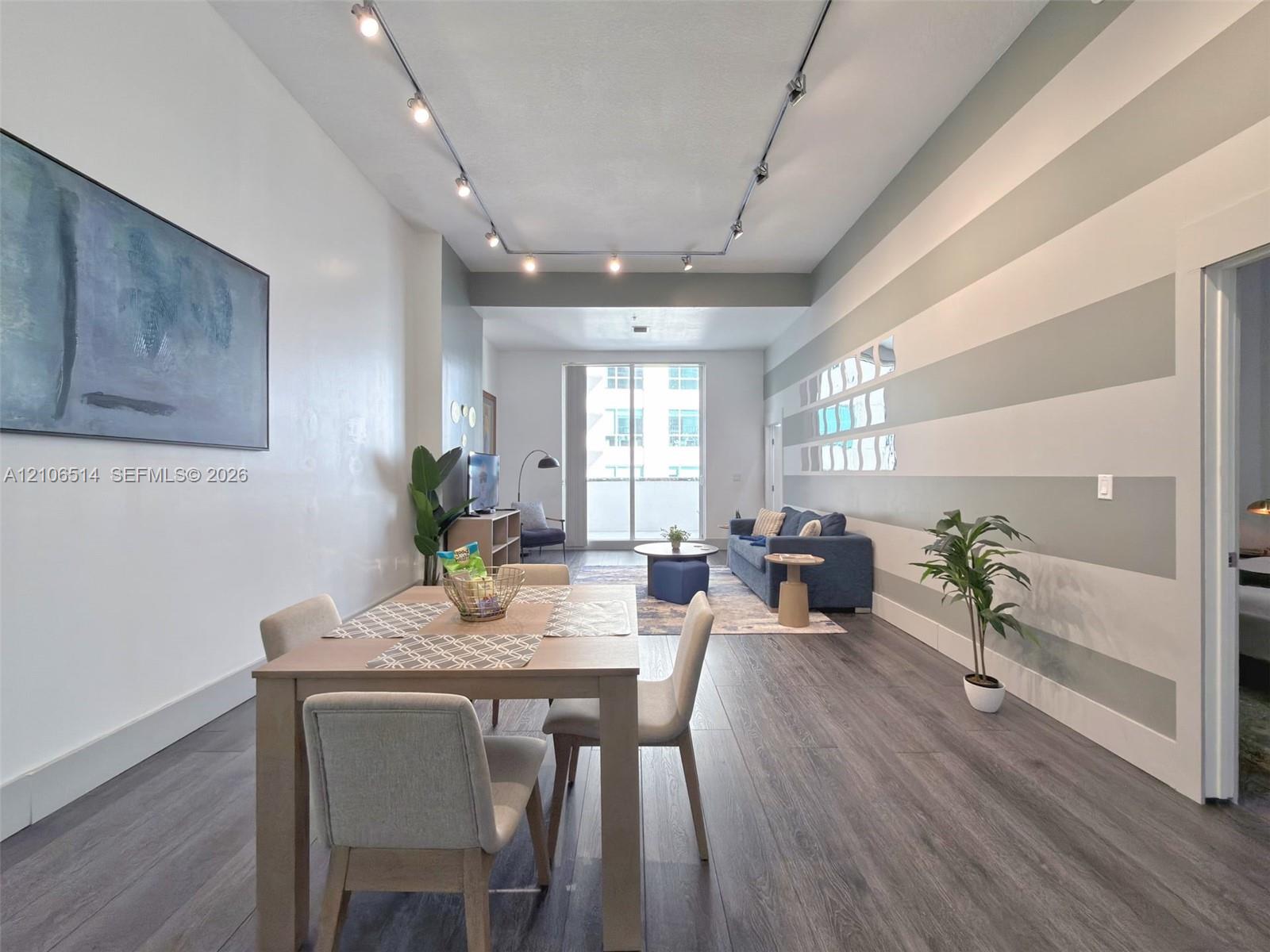 Open-concept interior featuring wood-finish flooring, high ceilings, ceiling-mounted track lighting, and a sliding glass door