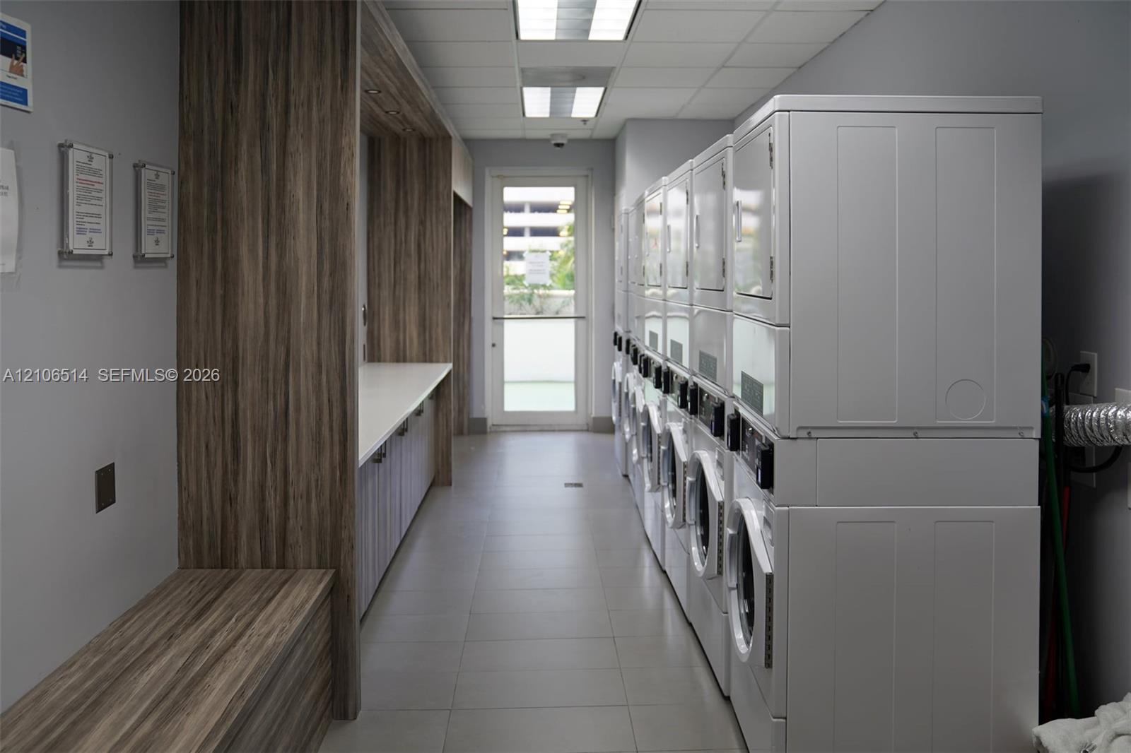 Laundry facility featuring stackable appliances, tile flooring, built-in wood-finish cabinetry, and solid-surface countertops