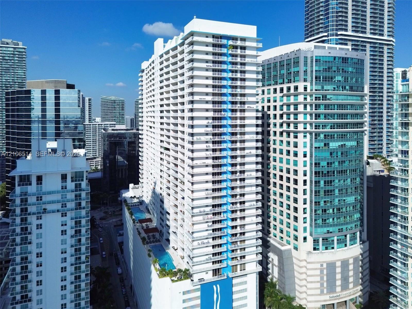 High-rise residential tower featuring multiple levels of private balconies, a multi-tier podium pool deck, and a distinctive blue architectural facade element