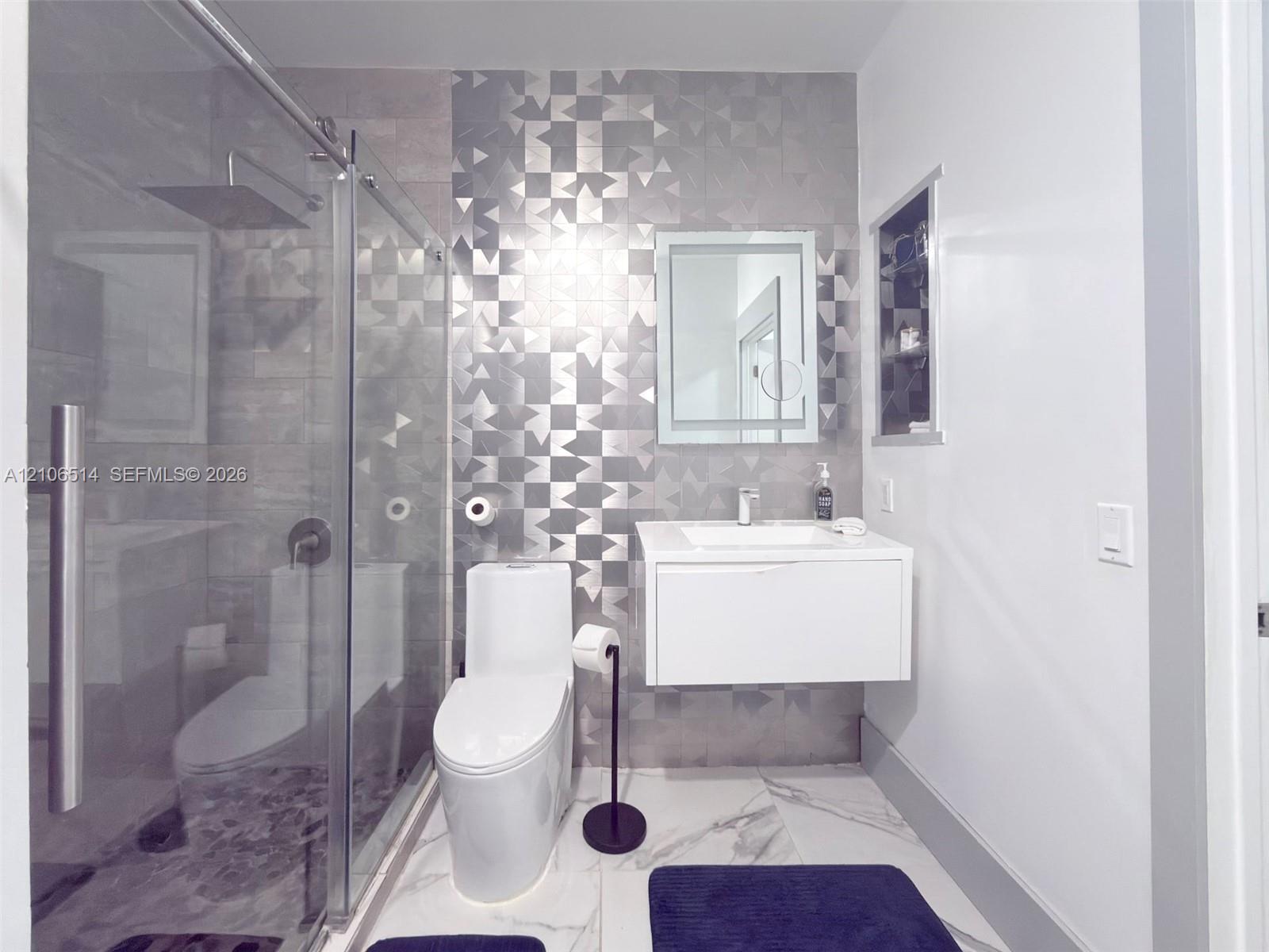 Floating vanity with integrated sink, walk-in glass-enclosed shower featuring a rainfall showerhead, geometric patterned accent tiling, and polished flooring