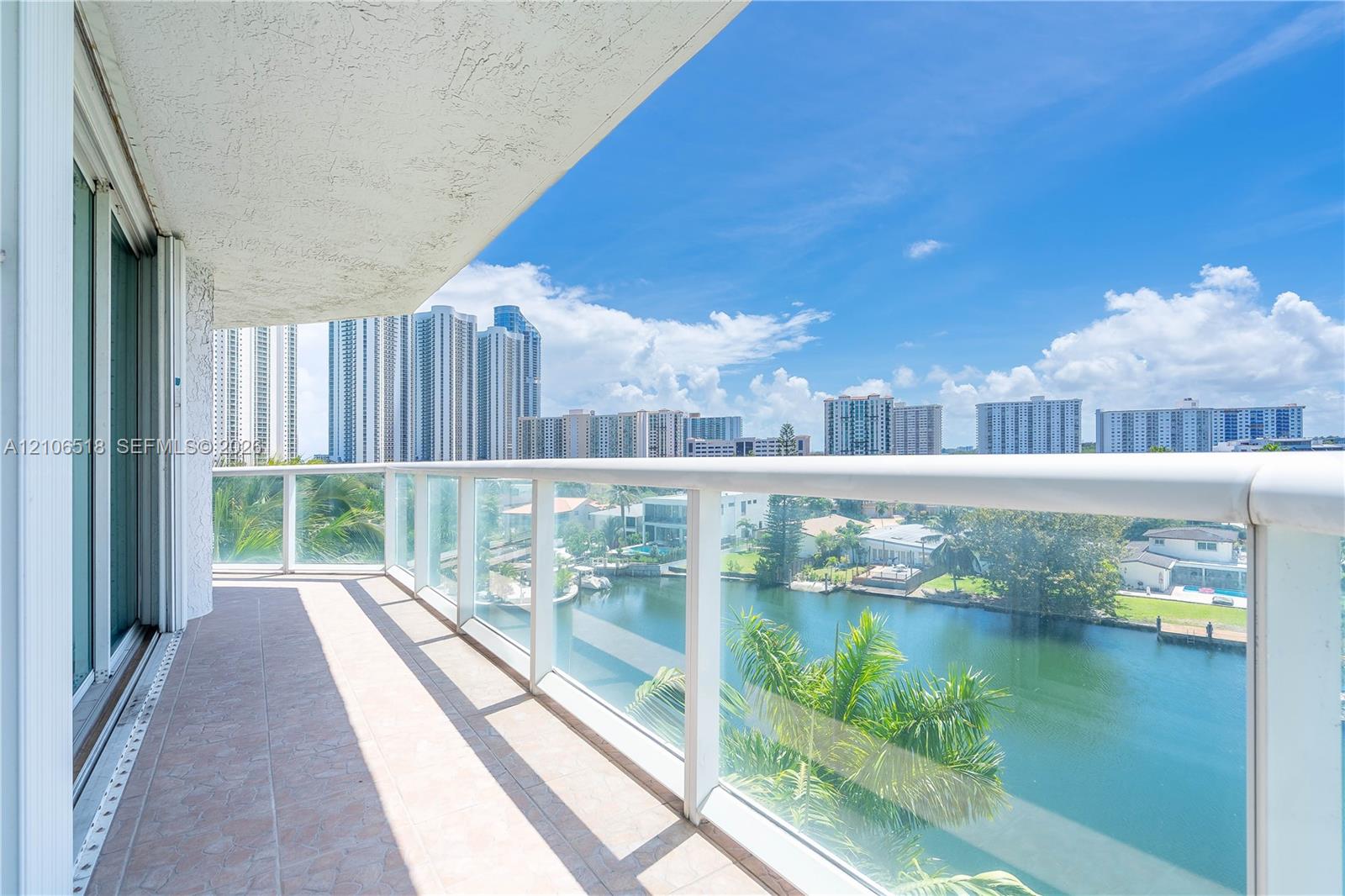 Covered balcony featuring tile flooring and a glass-paneled railing overlooking the waterway and cityscape