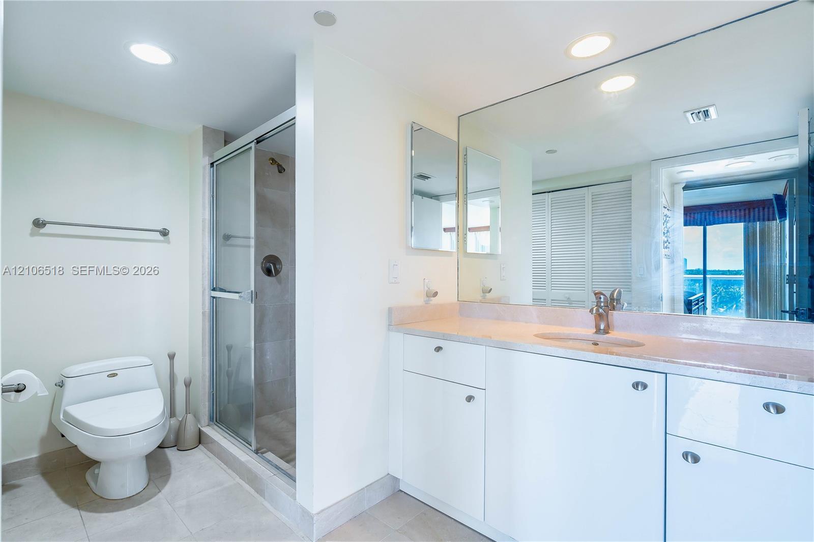 Bathroom featuring white cabinetry, solid-surface countertop, full-width wall mirror, glass-enclosed shower, and recessed lighting
