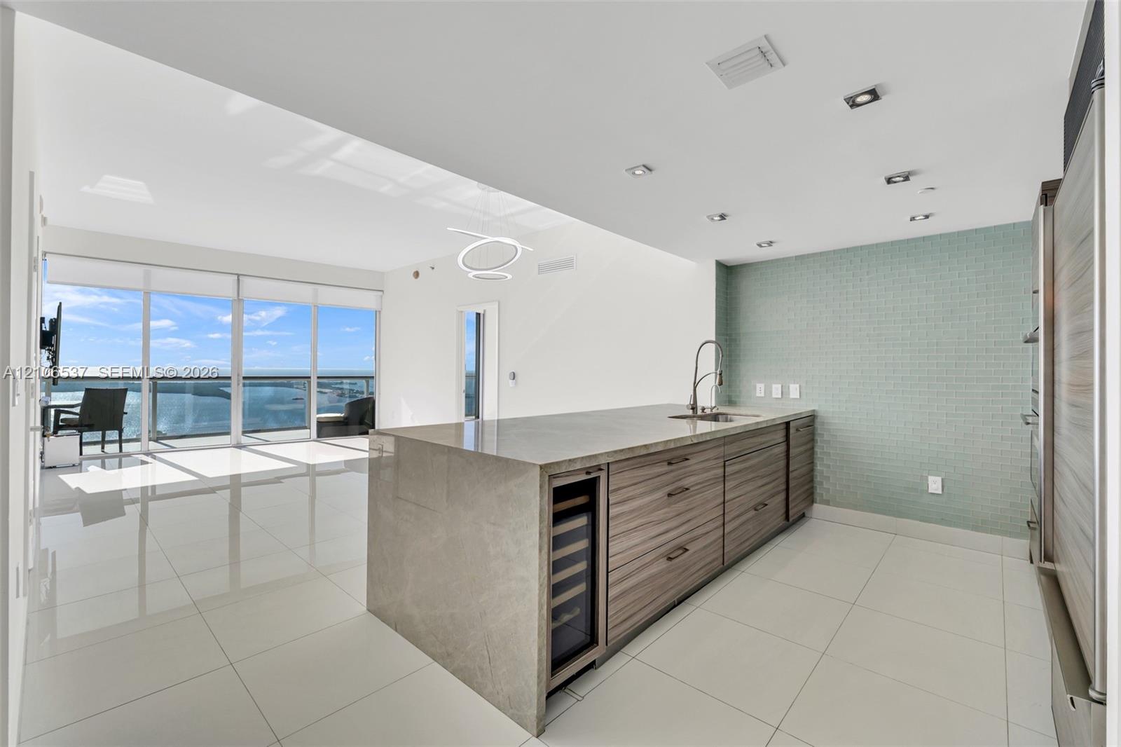 Kitchen island featuring stone countertop, wood-finish cabinetry, built-in wine refrigerator, glass tile backsplash, and floor-to-ceiling windows