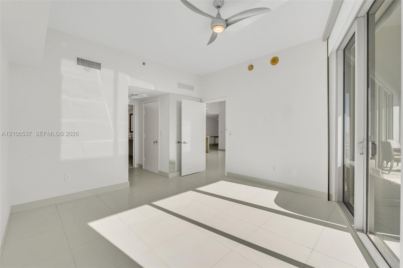 Neutral-toned interior featuring large-format tile flooring, a modern multi-blade ceiling fan, and expansive floor-to-ceiling glass sliding doors