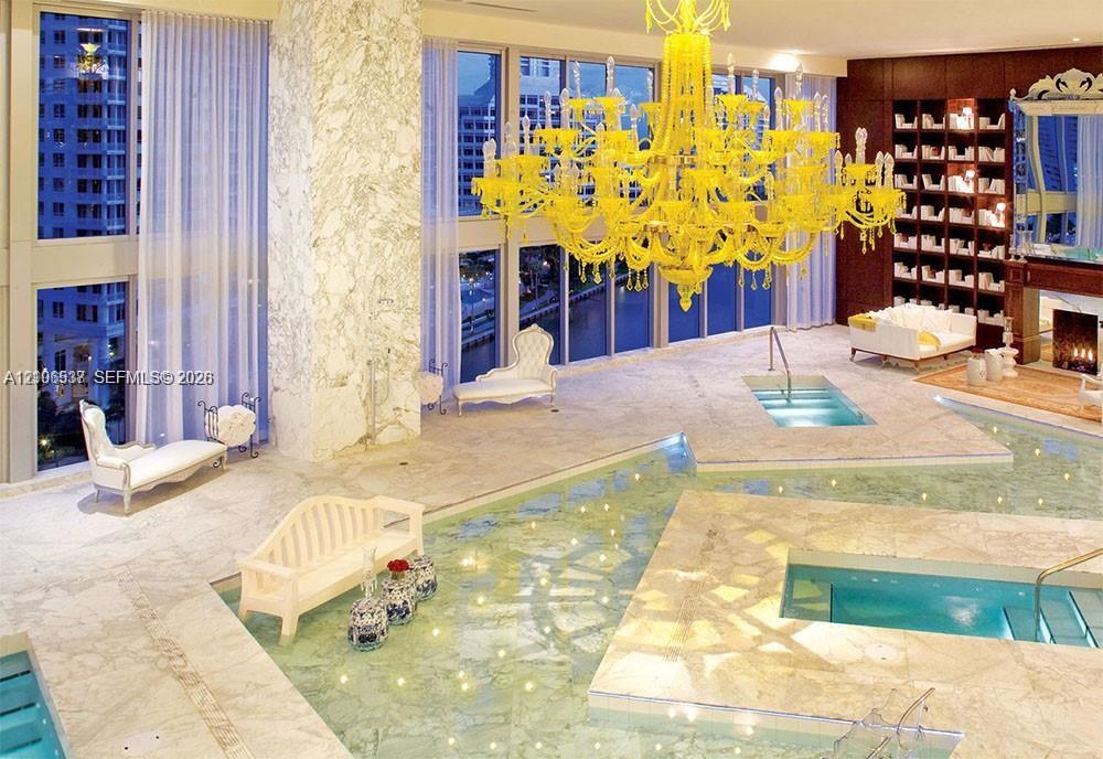 Floor-to-ceiling windows, stone flooring, integrated aquatic features, built-in shelving, and a prominent decorative chandelier