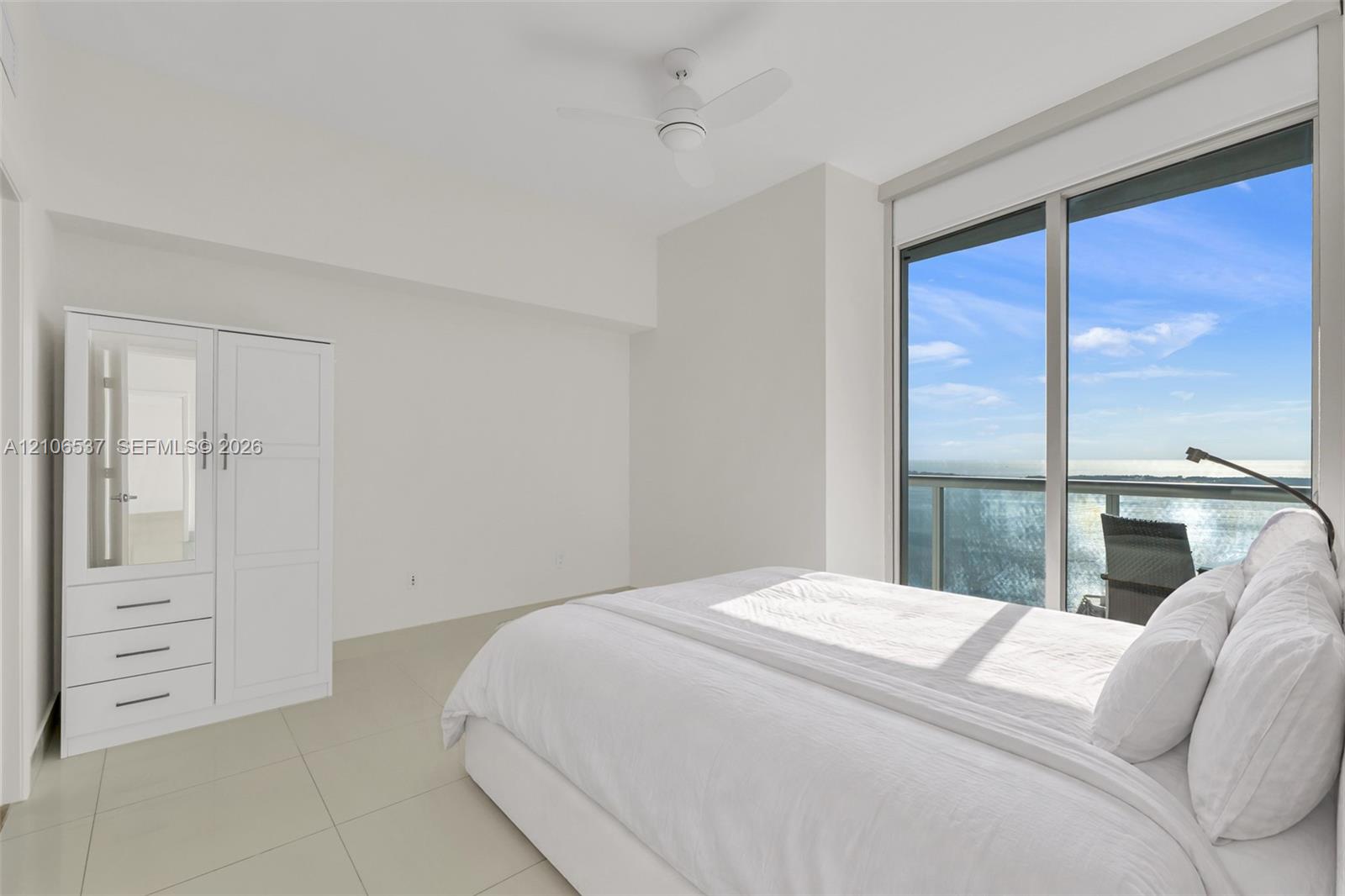 Floor-to-ceiling sliding glass doors, neutral tile flooring, built-in white cabinetry, and a ceiling-mounted fan