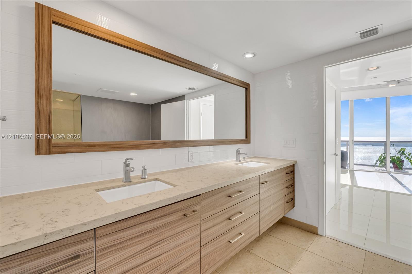 Dual-sink floating vanity with wood-finish cabinetry, stone countertop, integrated rectangular sinks, and an oversized wood-framed mirror