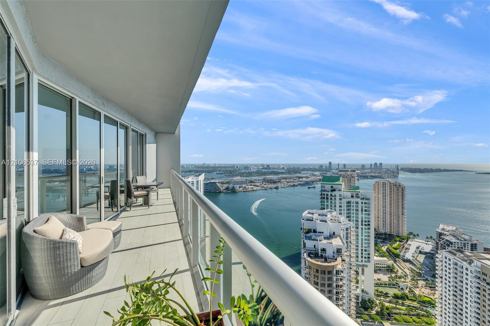 Covered terrace with porcelain tile flooring, full-height sliding glass doors, and a glass-paneled railing overlooking the waterway and cityscape