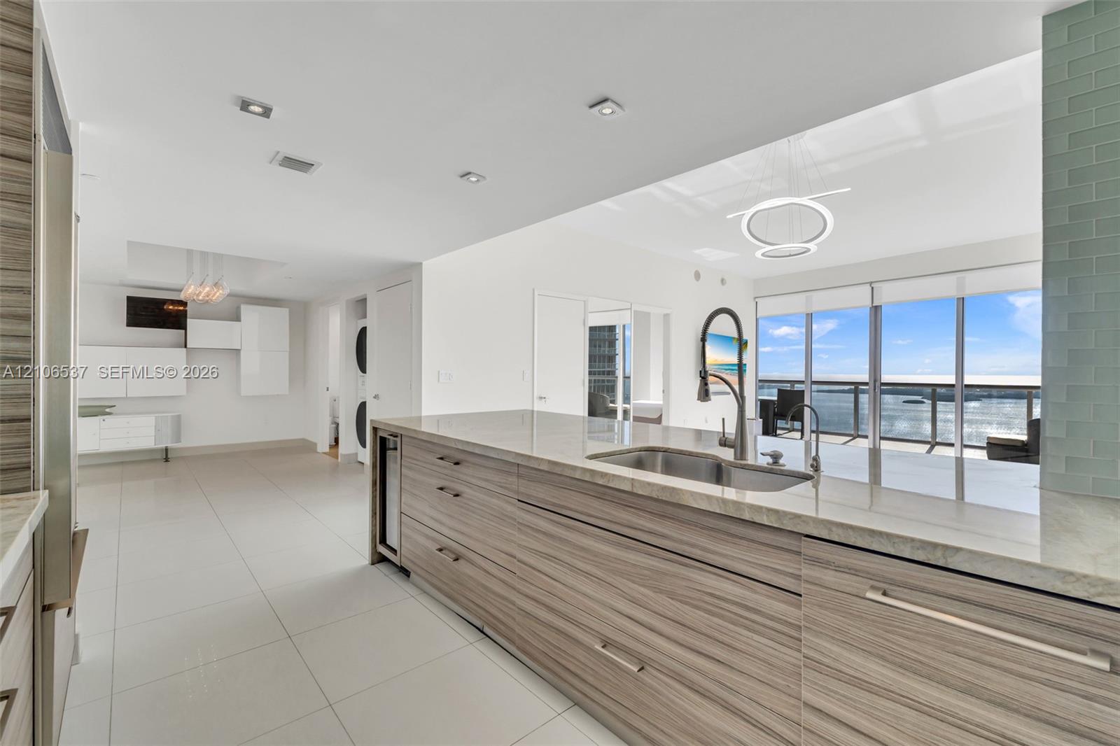 Kitchen featuring flat-panel wood-finish cabinetry, stone countertops, stainless steel undermount sink with a pull-down faucet, large-format tile flooring, and floor-to-ceiling windows