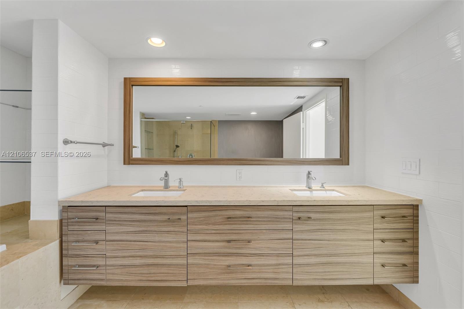 Floating vanity featuring wood-grain cabinetry, dual undermount sinks, stone-surface countertop, and a large framed mirror with integrated recessed lighting