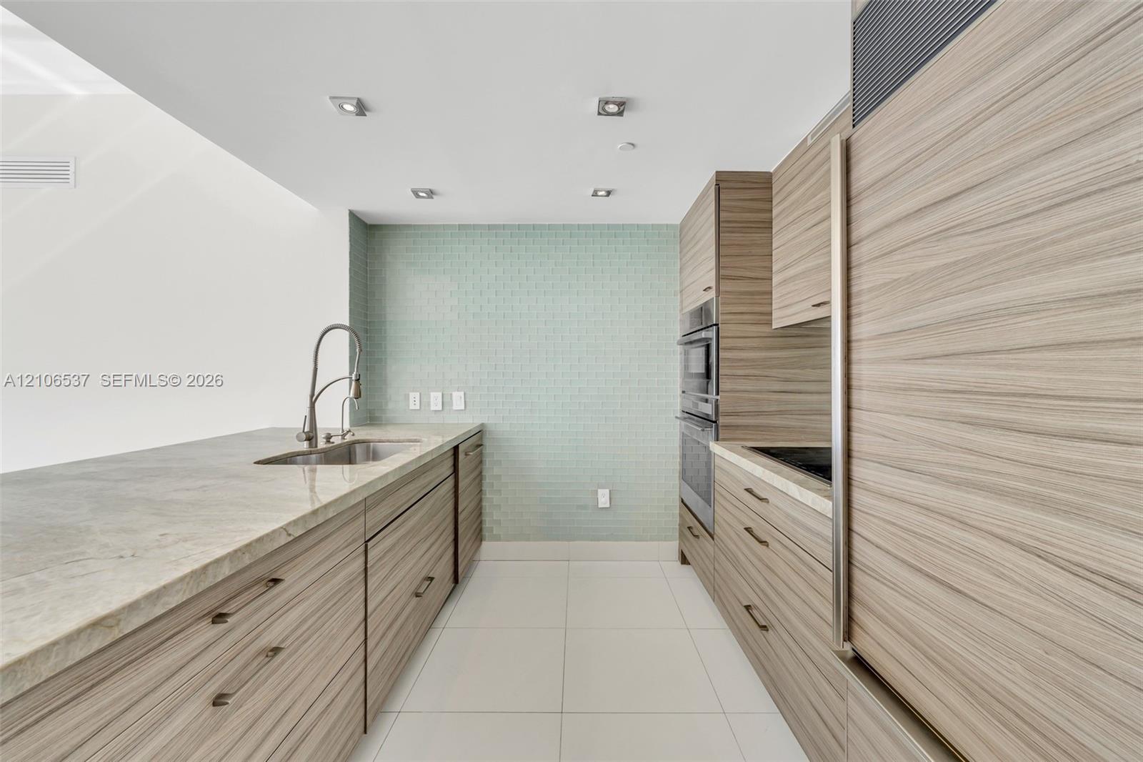 Kitchen featuring horizontal wood-grain cabinetry, stone countertops, integrated stainless steel appliances, a tile backsplash, and recessed lighting
