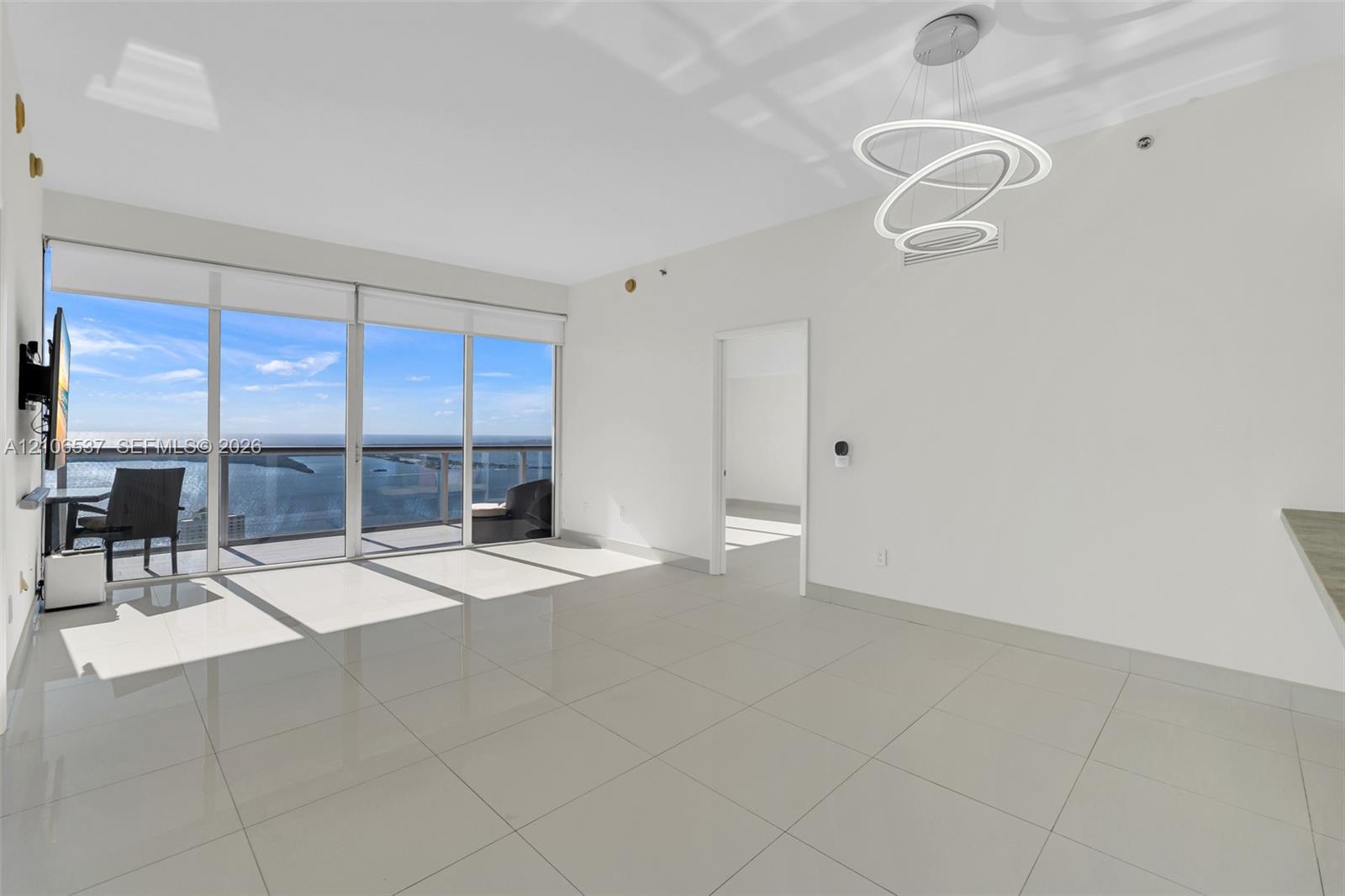 Living area featuring large-format tile flooring, floor-to-ceiling glass sliding doors, a metal-railing balcony, and a contemporary multi-ring LED chandelier