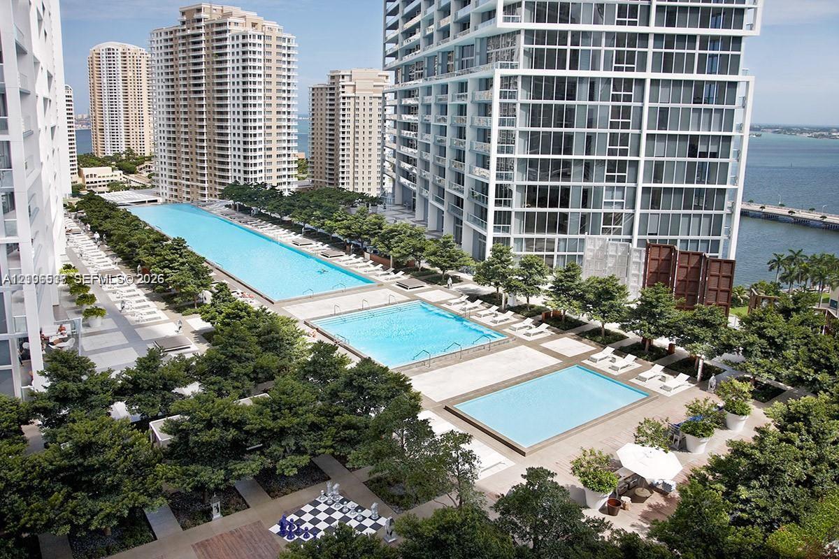 Elevated terrace deck featuring three distinct swimming pools, manicured tree-lined landscaping, stone-finish paving, and a built-in outdoor chess board