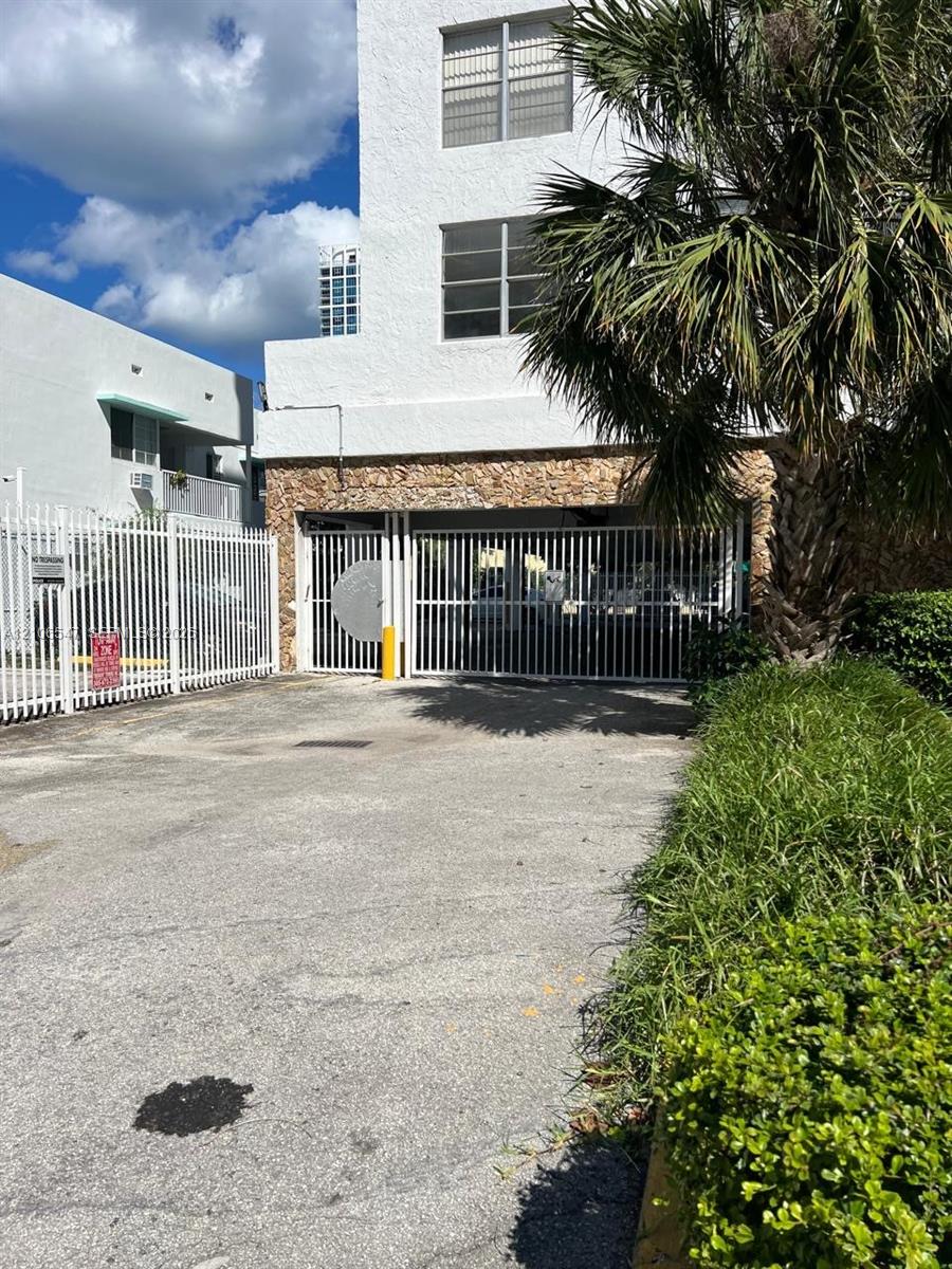 Exterior facade featuring a stone veneer base, white stucco finish, multi-level windows, secure gated parking entry, and perimeter fencing Exterior facade featuring a stone veneer base, white stucco finish, multi-level windows, secure gated parking entry, and perimeter fencing