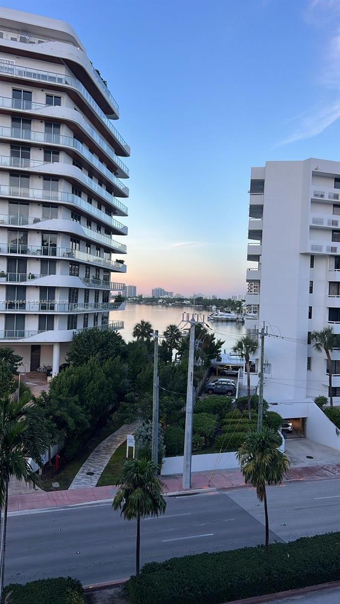 High-rise residential exterior with glass panel balconies, surrounded by mature palm trees and coastal waterway